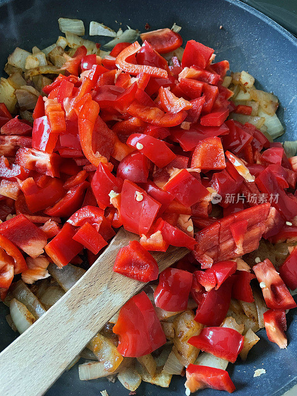 木勺在不粘煎锅里搅拌蔬菜，用香料烹制切碎的红甜椒和白洋葱丁，画面优美