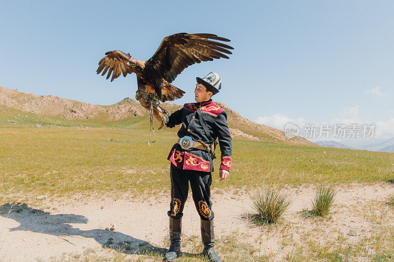 在中亚山区，身穿传统服装的老鹰猎人和老鹰在一起