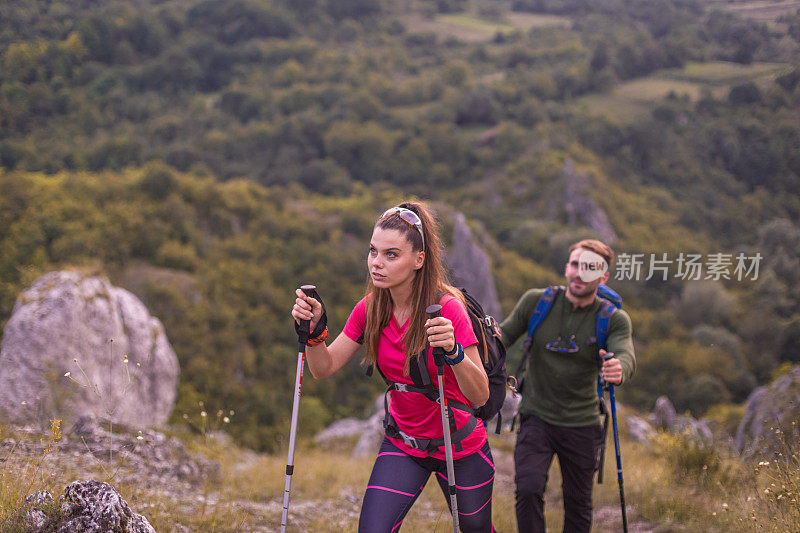 年轻的男女夫妇带着专业的装备和登山杆在美丽的大自然中徒步旅行