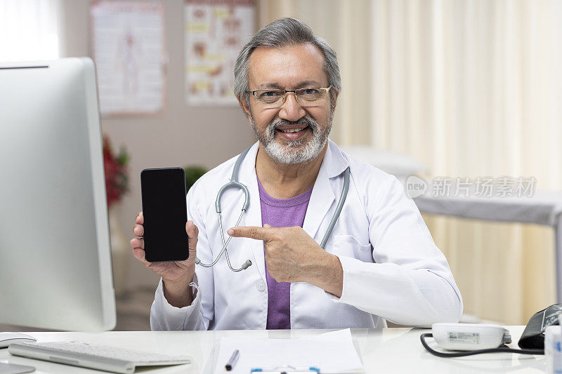 一个成熟的男性医生在他的诊所里显示一个空白的手机屏幕