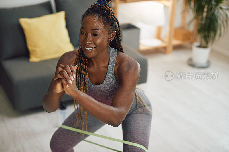 快乐的黑人运动女性在做深蹲，腿上缠着抵抗带。