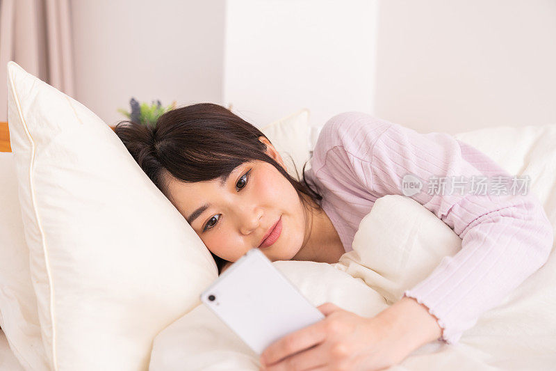 漂亮的亚洲女人在床上用智能手机