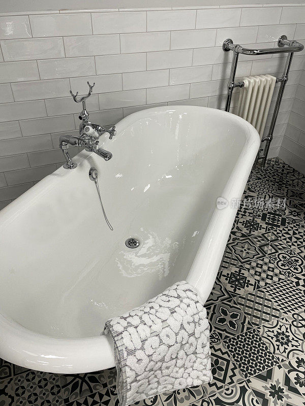 维多利亚风格的豪华浴室套房的特写图像，白色陶瓷独立弯曲卷顶浴缸与金属爪脚，铬，浴缸淋浴龙头，纹理毛巾，黑白图案地砖