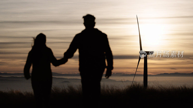 一对夫妇在云雾缭绕的山峰上享受着风力发电机附近的日落。可持续性。