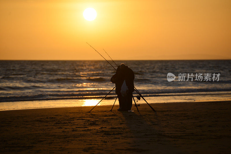 夕阳西下，空荡的海滩上的渔夫，夕阳映衬着他和他的钓竿，营造出一种宁静祥和的景象。