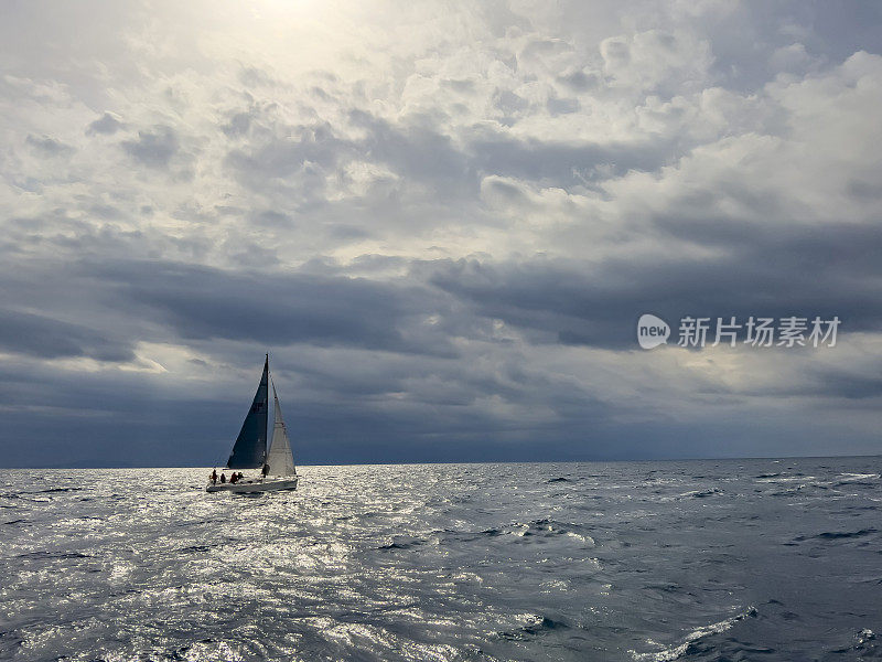 一艘帆船和船员在多云的日子里航行，灰色的天空和大海的背景