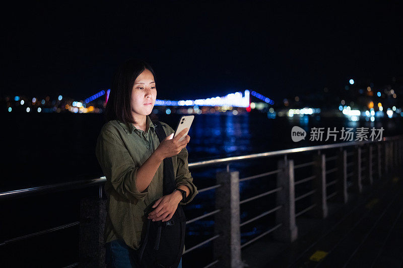 年轻女性游客晚上在城市里使用智能手机