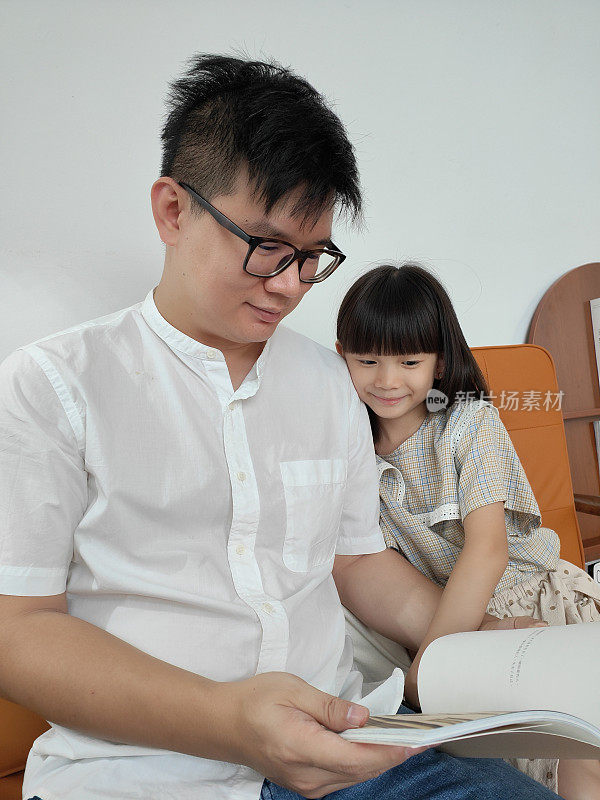幸福的家庭亚洲华人父亲和孩子女儿在客厅读故事书。
