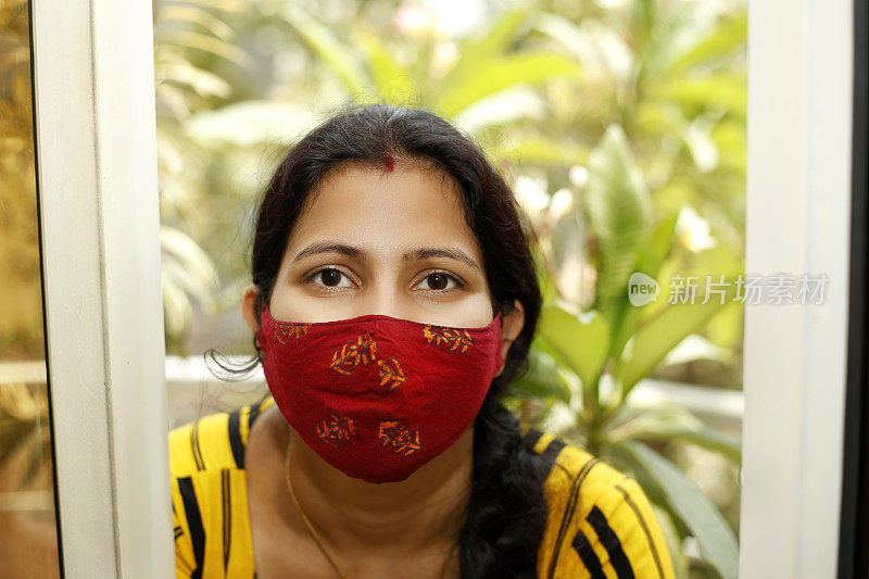 年轻的印度女子站在阳台上，用防污染口罩遮住脸