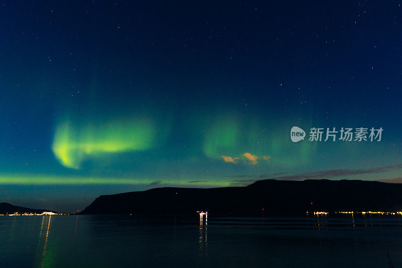 风景秀丽的北极光在峡湾和发光的城镇在挪威