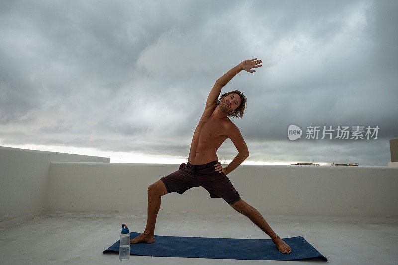 健康的年轻人在做瑜伽，他在户外的屋顶上练习，背景是风暴云