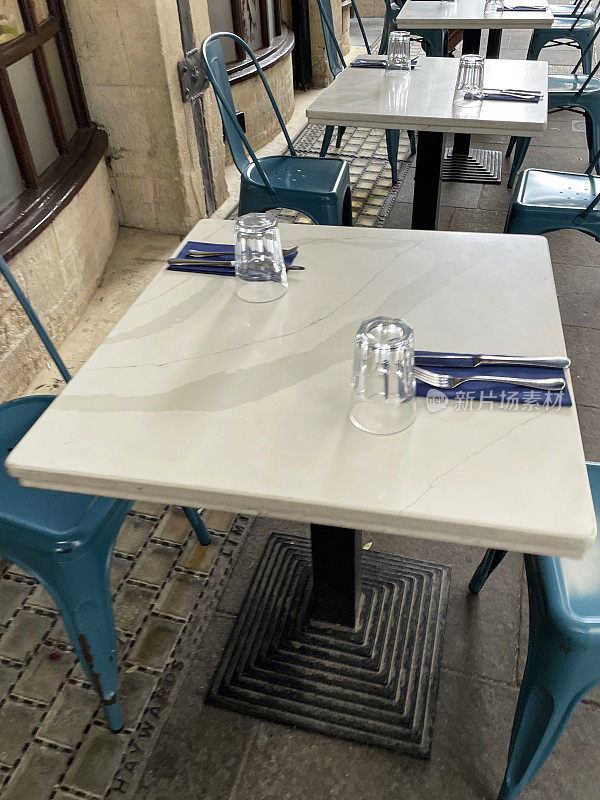 广场的特写图像，露天咖啡馆的大理石桌子与蓝色，塑料，小酒馆的椅子在街道铺就的露台用餐区，高架的视野，重点在前景