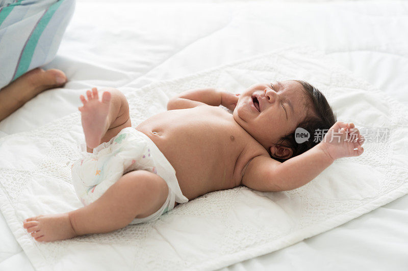 新生婴儿在白色的床上盖着毯子睡觉时啼哭。亚洲新生儿啼哭