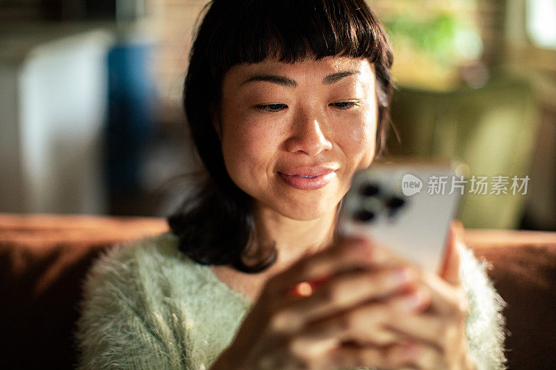 年轻的日本女子在沙发上使用智能手机