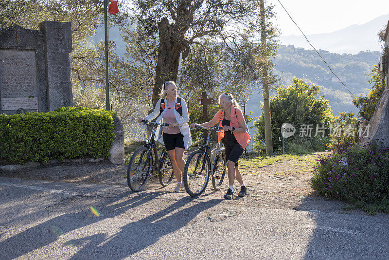 年长的女自行车手推着自行车沿路前行