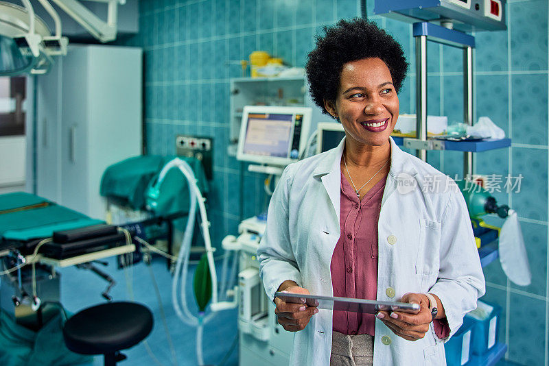 一位面带微笑的非洲医生在手术室里拿着电子平板电脑。