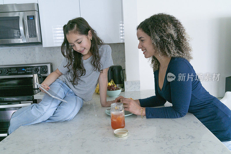 母女俩一边准备早餐，一边在家的厨房里开心地看着平板电脑