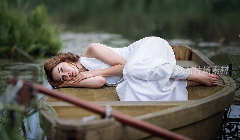 一个漂亮的年轻女人的肖像躺在河岸边的船上。