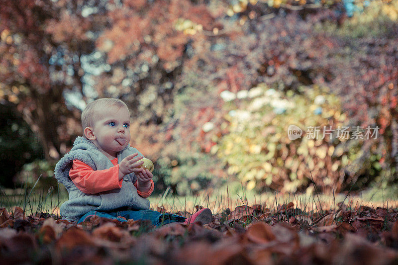小女孩一边吃着绿苹果，一边在树叶间玩耍