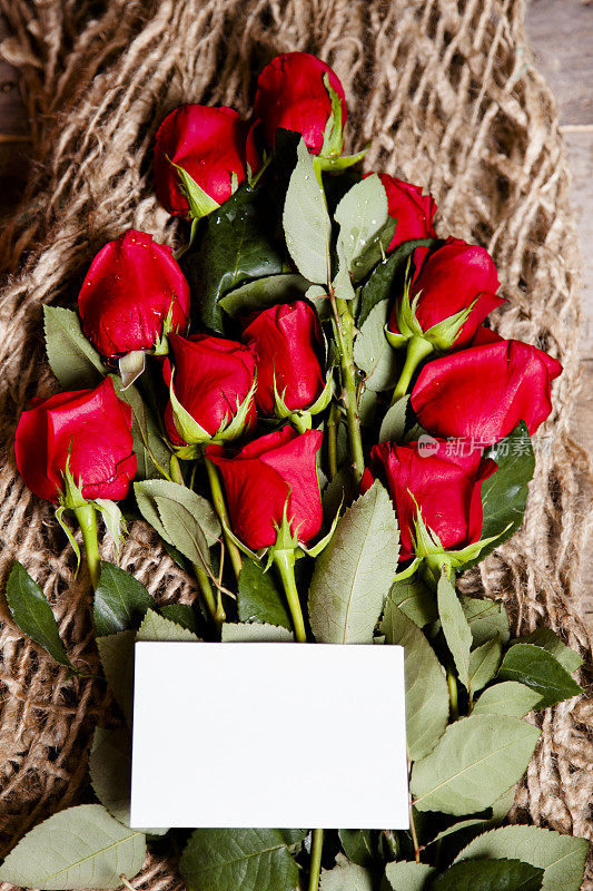 情人节。红玫瑰花束，空白卡片。乡村的木桌上。