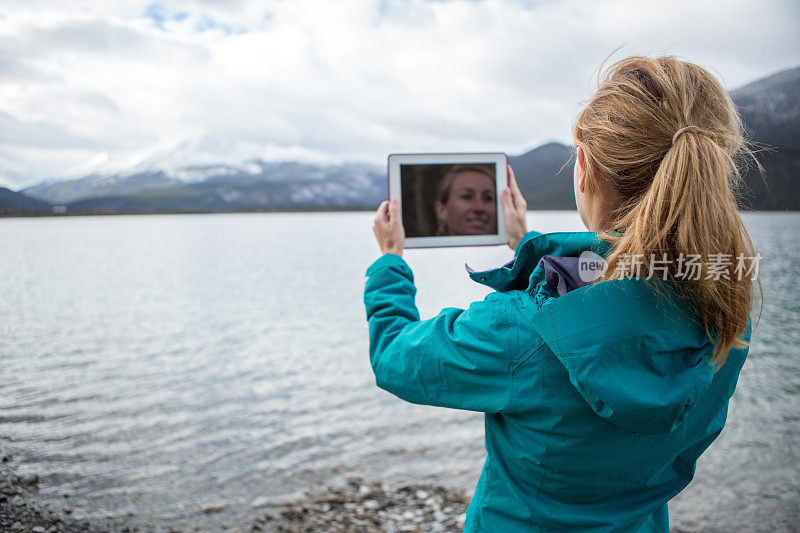 年轻女子在湖边用数码平板电脑拍照