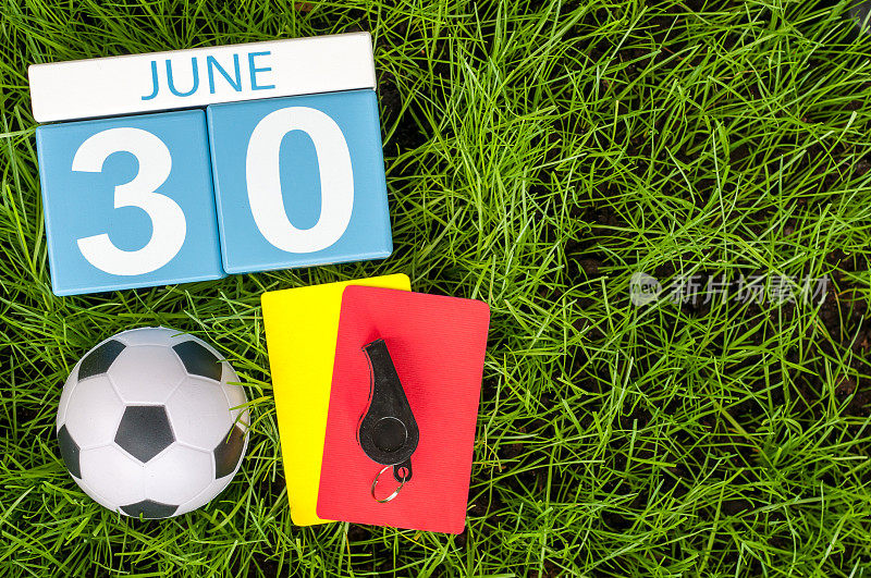6月30日。6月30日的图片木制彩色日历在绿色草地的背景与足球装备。夏天的一天