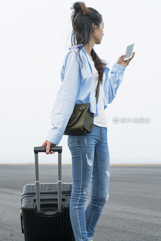 年轻女子拿着行李箱走路，用手机打电话