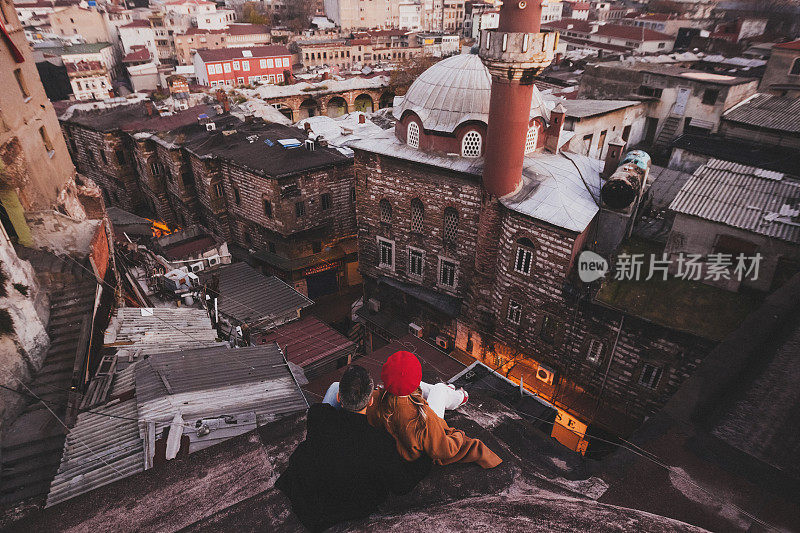 相爱的夫妇坐在屋顶上欣赏伊斯坦布尔的夜晚。休闲风格，秋风，红色贝雷帽和米色外套