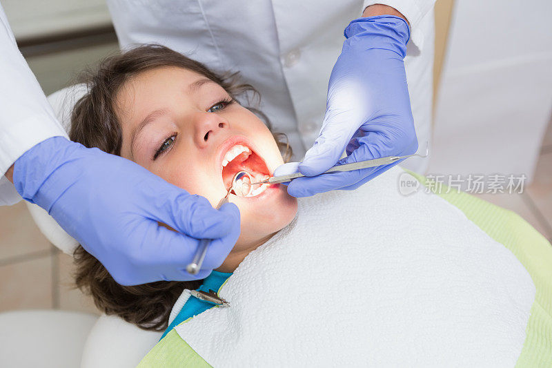 儿科牙医在牙医的椅子上检查一个小男孩的牙齿