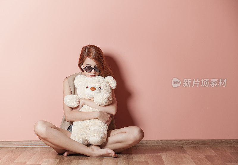 美丽的年轻女子抱着泰迪熊坐在墙边的照片
