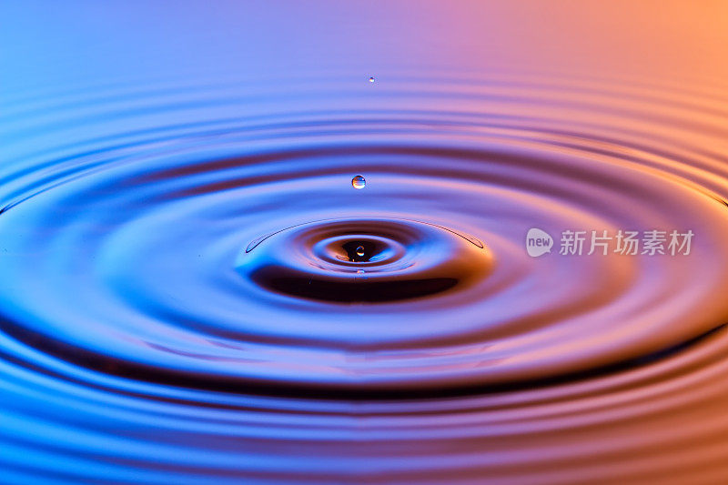 水滴近距离与同心涟漪在五颜六色的蓝色和琥珀表面
