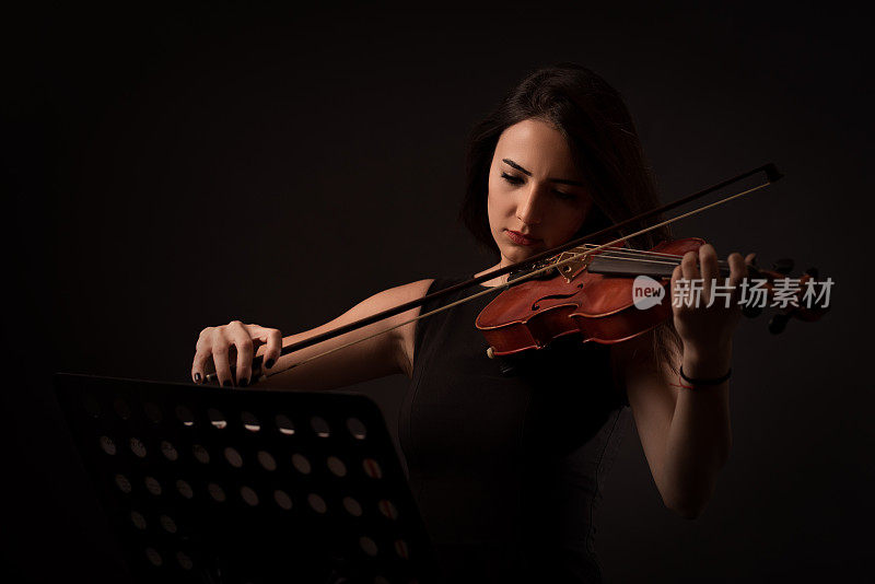 美丽的年轻女子在黑色的背景上拉着小提琴