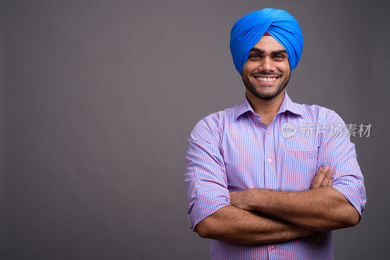 在灰色背景下，年轻英俊的印度男子戴着头巾