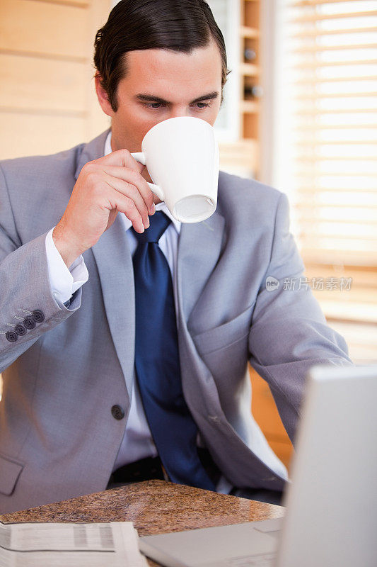 一个商人在他的笔记本电脑旁喝了一口咖啡