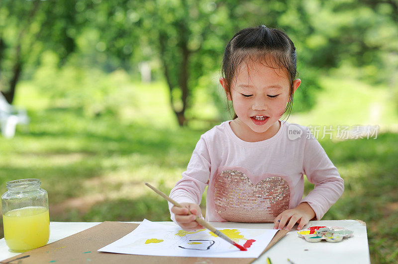 孩子坐在桌子上，在绿色的花园里画美术纸。
