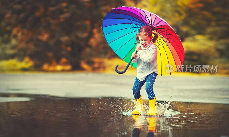 快乐有趣的孩子女孩与伞跳在水坑在橡胶靴子