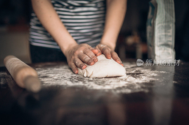 手用擀面杖在木桌上烘烤生面团