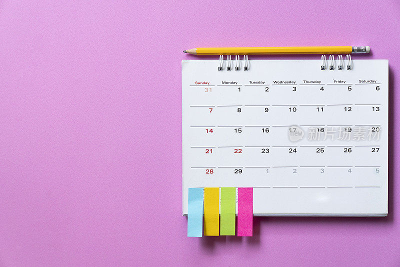 近距离的日历放在粉红色的桌子上作为背景，计划商务会议或旅行的计划概念