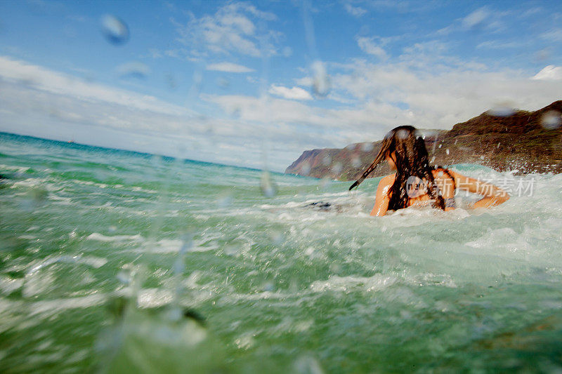 在夏威夷的海滩上，水溅在一个青少年游泳者身上