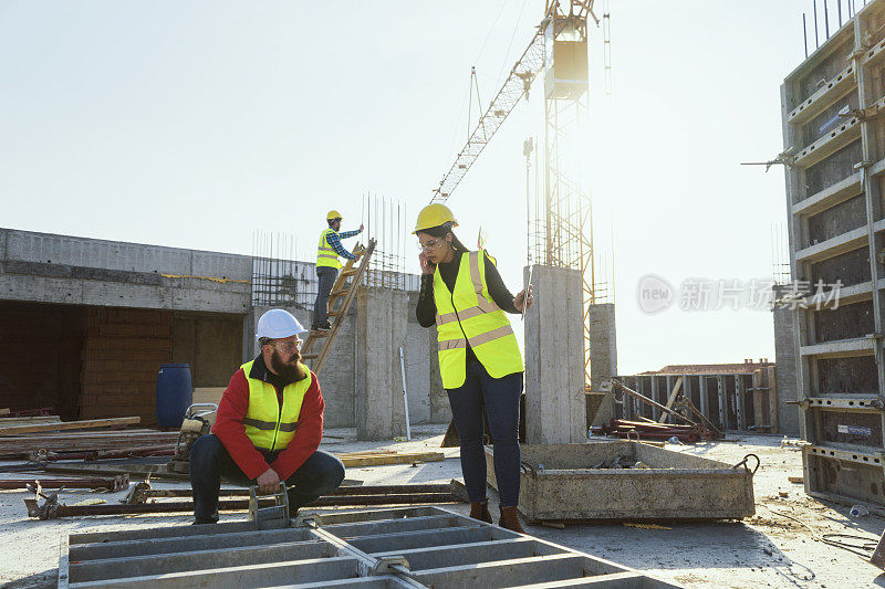 一个阳光明媚的日子，一位自信的女建筑师拿着平板电脑和一位建筑工人在一个住宅楼的工地上一起讨论和工作。