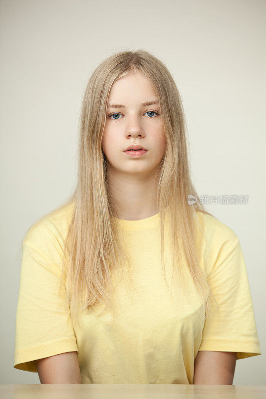 一个金发少女的工作室肖像在黄色t恤坐在桌子上的米色背景