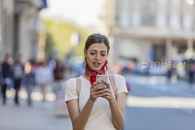 一名年轻女子正带着她的智能手机走在城市的路上