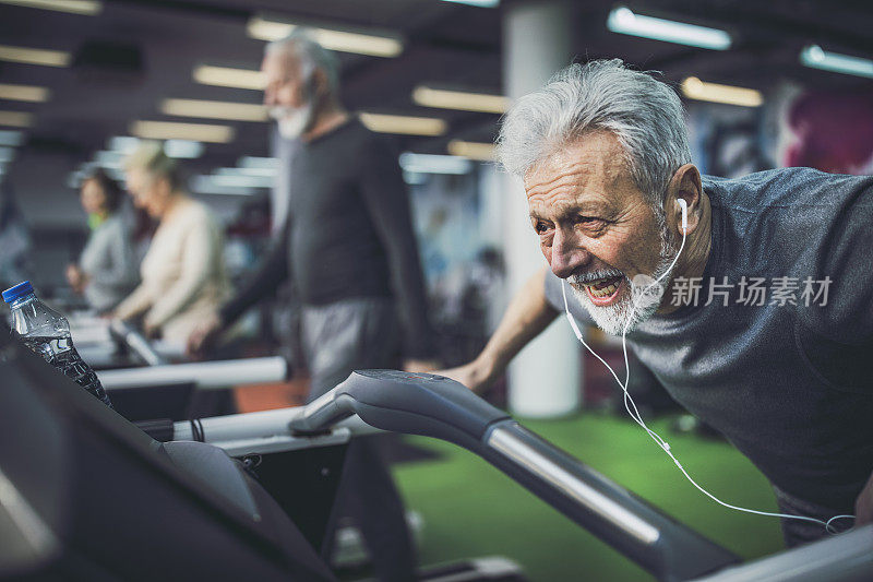 精疲力竭的老人在健身房里的跑步机上听音乐。