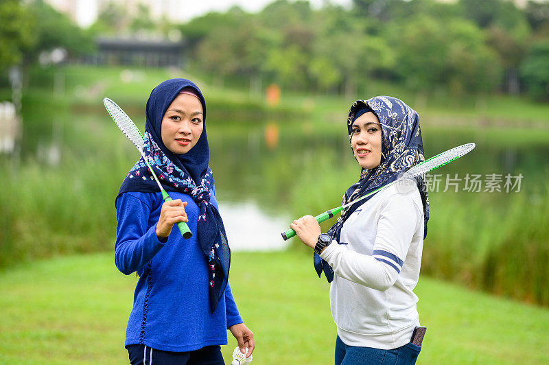 两名亚洲穆斯林妇女戴着头巾在公园打羽毛球