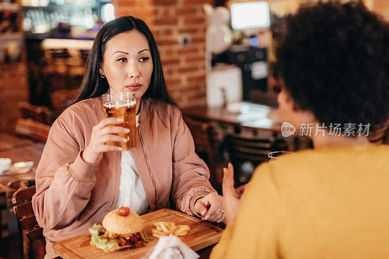 两个中年妇女在酒吧里享受啤酒和汉堡