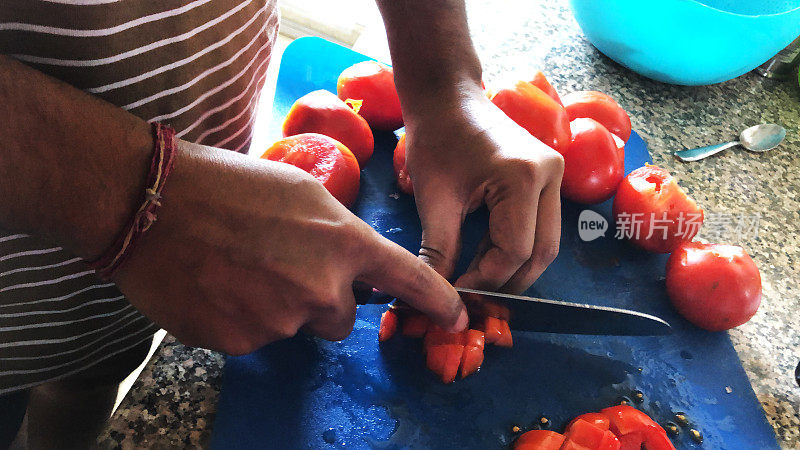 一个不认识的男人在家庭厨房的菜板上切着番茄，一个男人拿着锋利的刀切着番茄，切碎的番茄用来做意大利面酱，戴着手镯