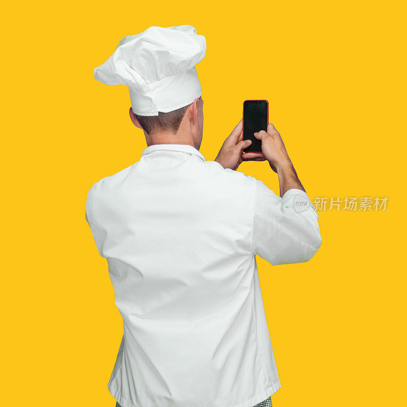 白人男厨师穿着制服站在黄色背景前发短信