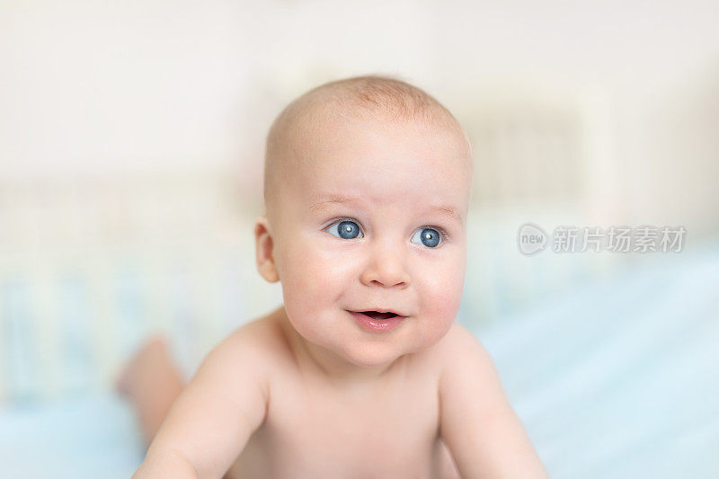 可爱可爱的5个月大的白人小男婴躺在育婴室的床上，开心地玩耍和微笑。快乐健康的新生儿概念。有趣的幼儿特写肖像