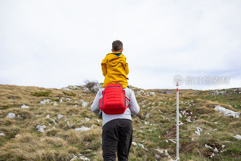 一个男孩骑在他父亲的肩膀上在山里徒步旅行
