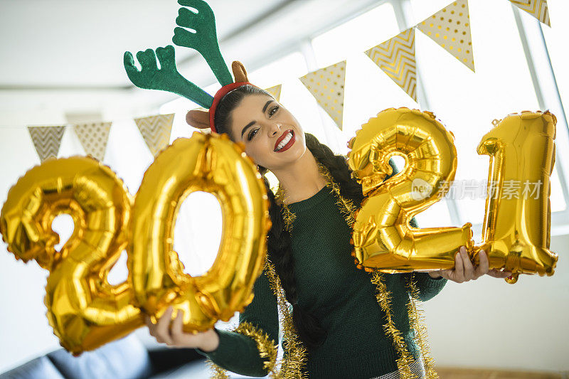 美丽的女人在新年派对上玩得很开心，拿着气球数字2021，代表即将到来的新年